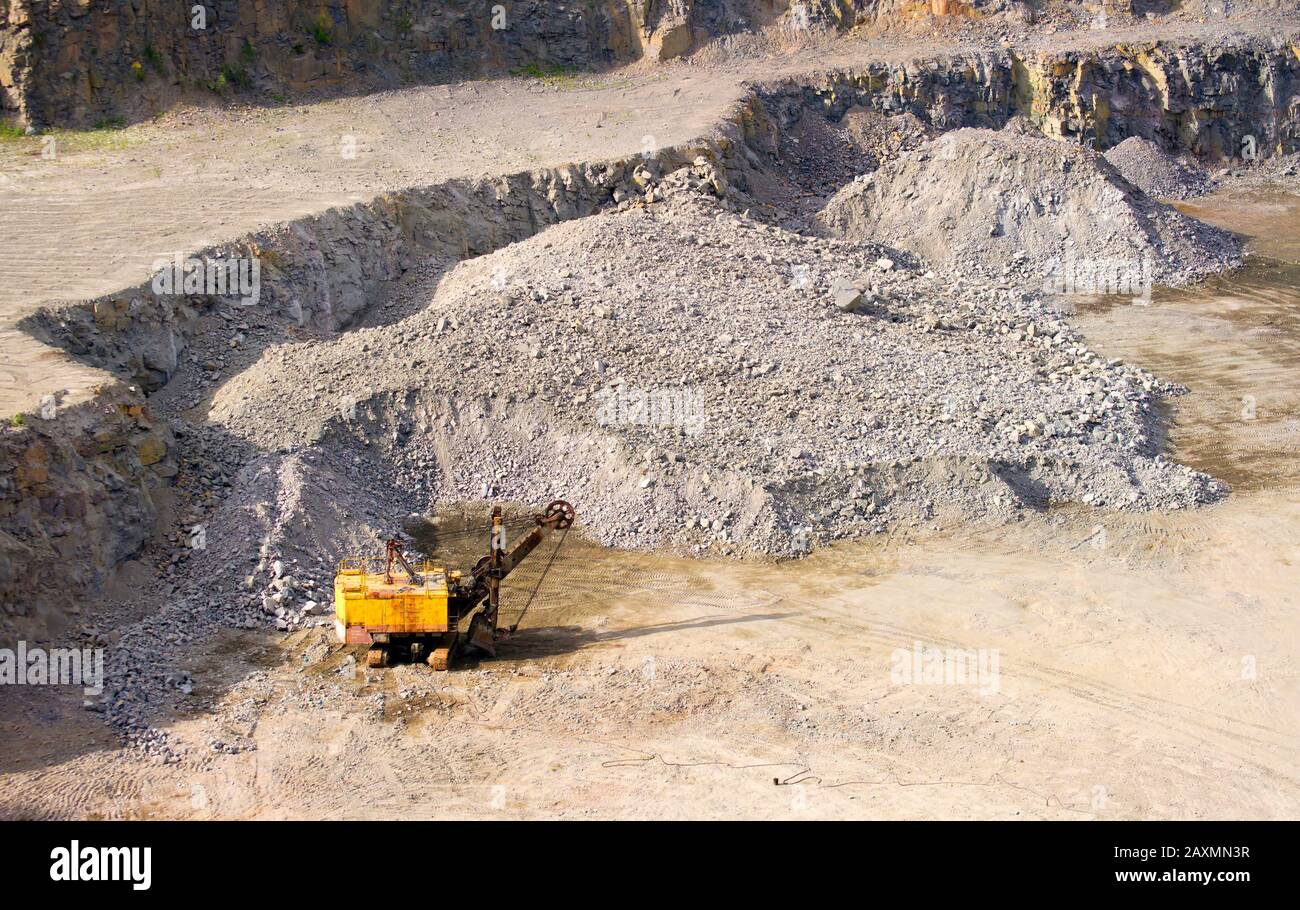 macchina escavatore giallo macerie di scalpellatura vicino alle rocce in una cava per l'estrazione del granito Foto Stock