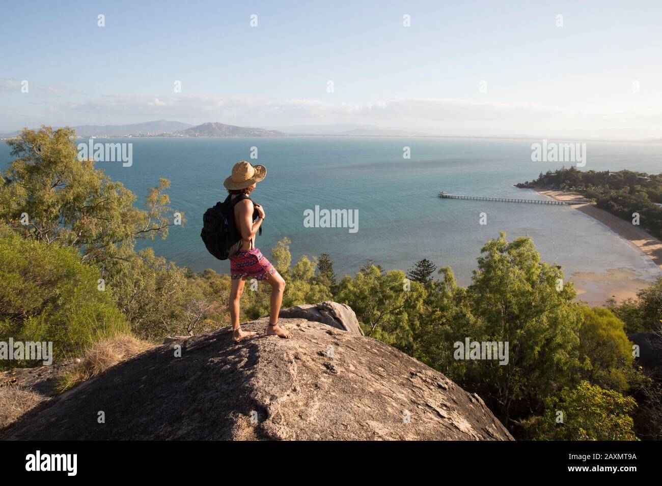 Zaino con cappello e costume da bagno, in cima a una collina rocciosa durante il tramonto Foto Stock