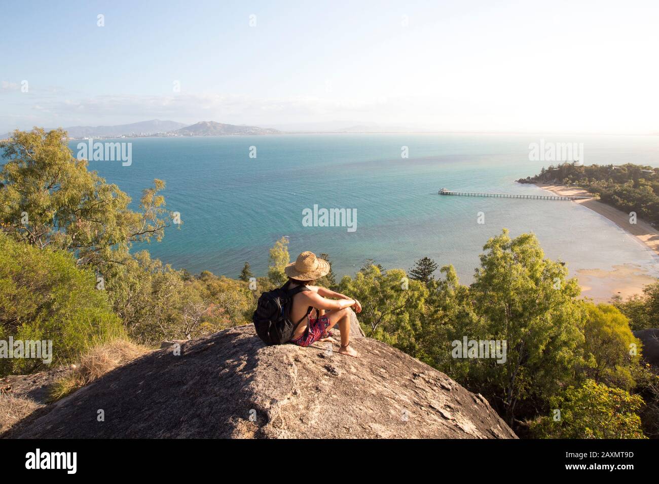 Zaino con cappello e costume da bagno, in cima a una collina rocciosa durante il tramonto Foto Stock