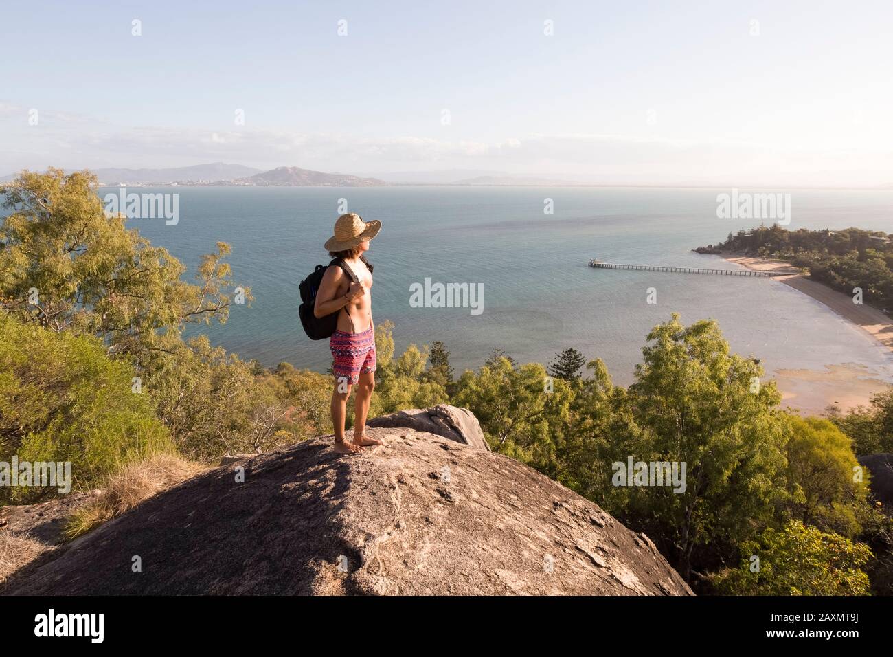 Zaino con cappello e costume da bagno, in cima a una collina rocciosa durante il tramonto Foto Stock