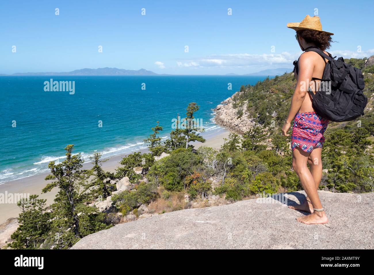Giovane zaino in spalla con cappello e costume da bagno, con vista sull'oceano Foto Stock