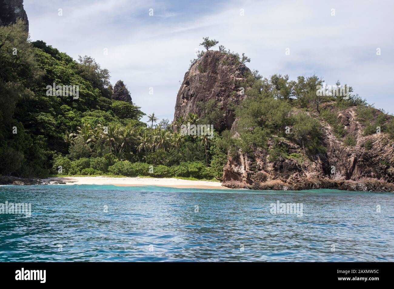 Isolata piccola spiaggia di sabbia tropicale, circondata da palme e roccia Foto Stock