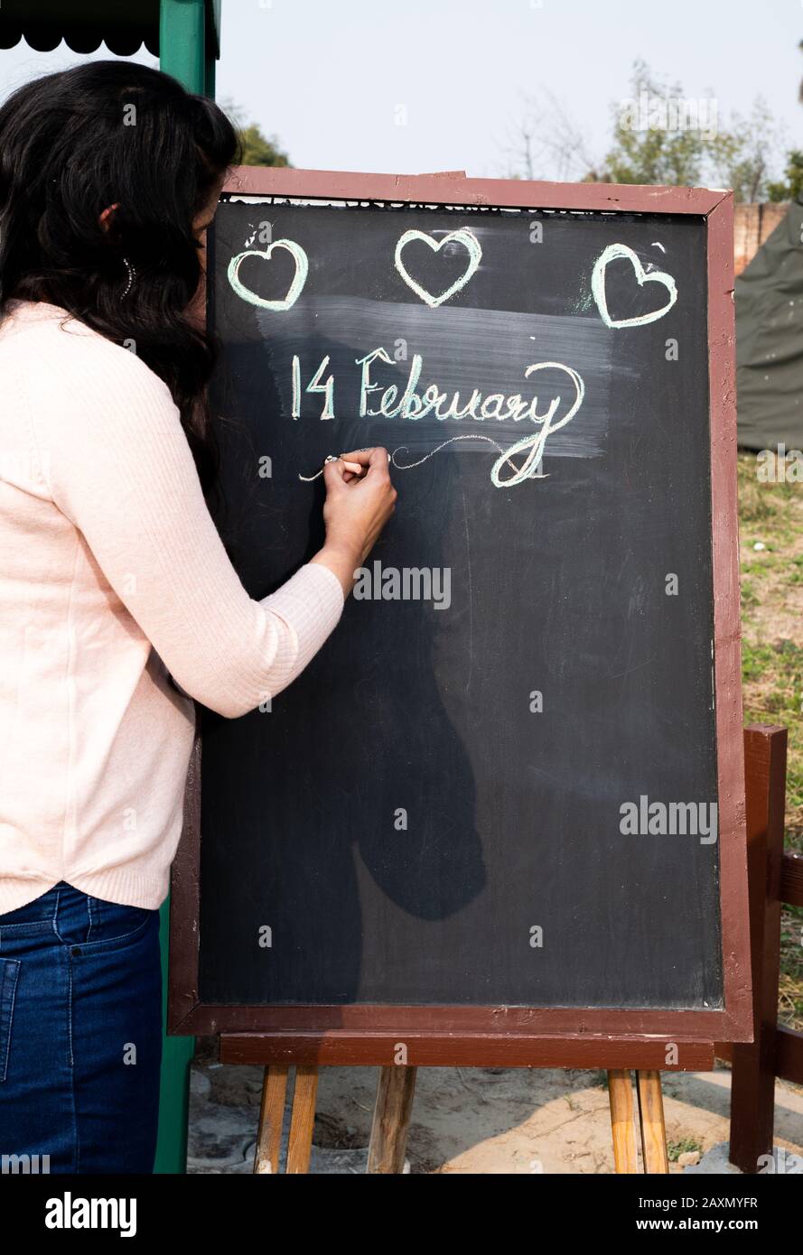 Ragazza Che Scrive San Valentino Su Blackboard O Bacheca Di Avviso Con I Cuori Foto Stock