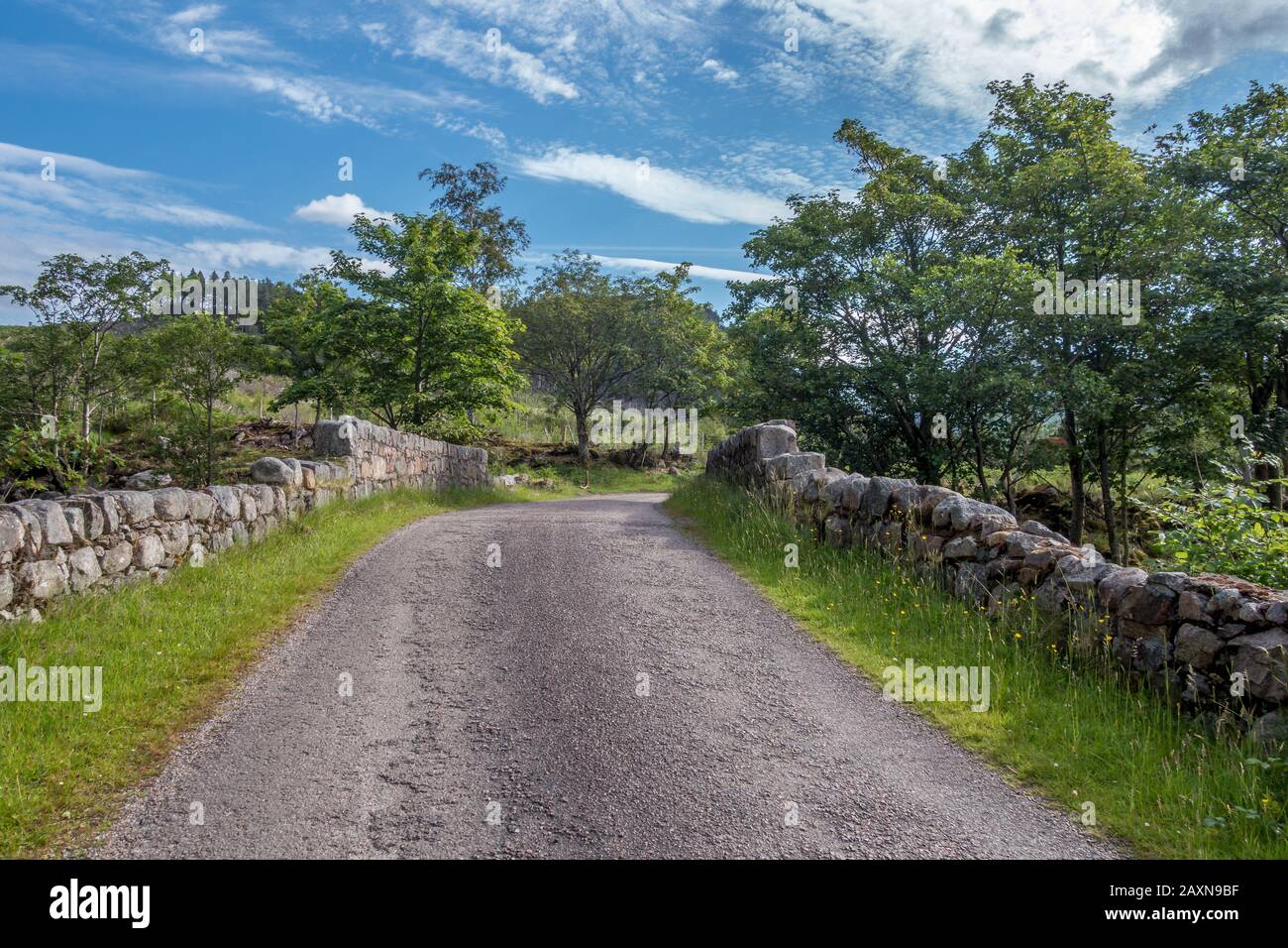 Strada lastricata nella valle di Glen Etive nelle Highlands scozzesi che conduce attraverso un vecchio ponte di pietra con pareti di pietra sui lati in estate Foto Stock