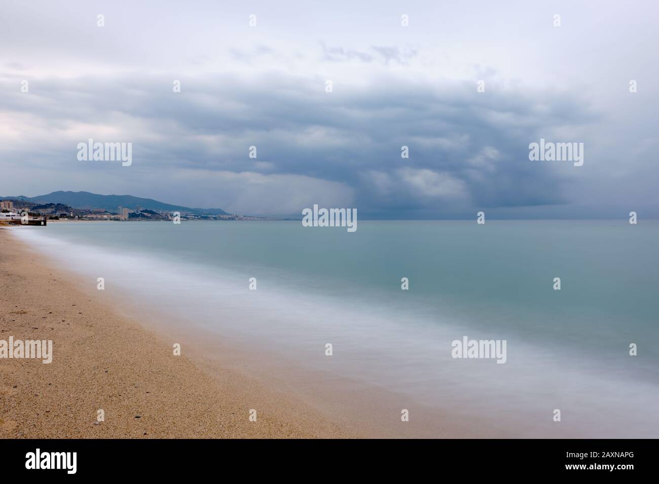 Lunga esposizione sulla spiaggia con sabbia dorata e una tempesta in lontananza, Badalona Foto Stock