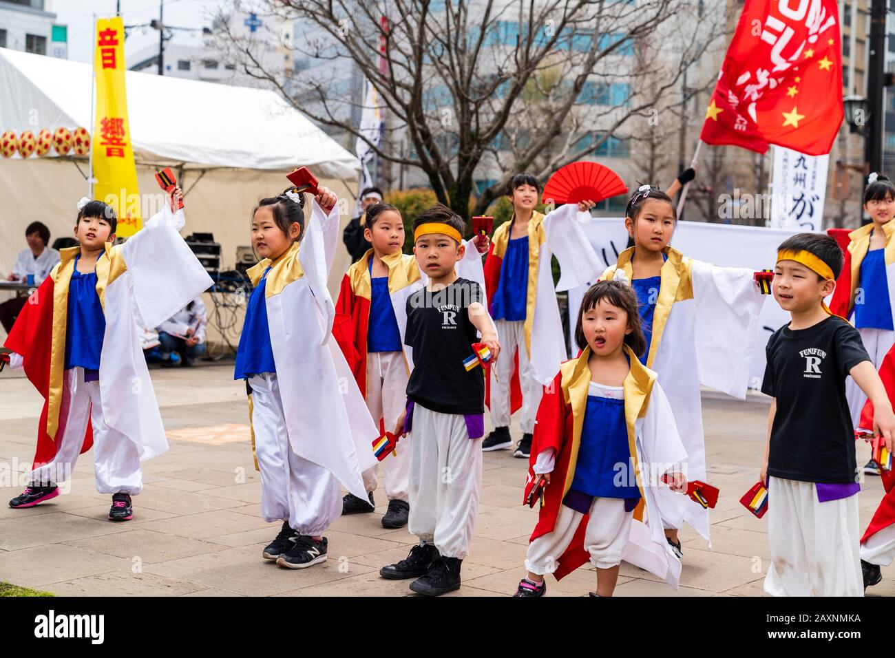 Ballerini di Yosakoi, bambini piccoli, balli con naruko, clappers, all'aperto al festival Kyusyu Gassai, Kumamoto. Uomini che ondeggianti banner in background. Foto Stock