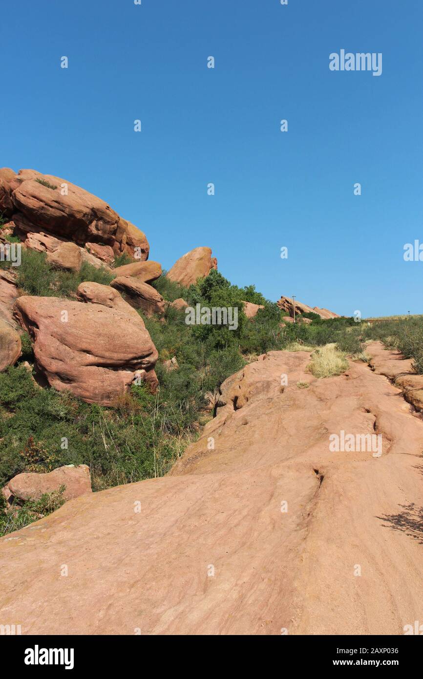 Il Trading Post Trail accanto a grandi formazioni rocciose di arenaria rossa con arbusti che crescono nelle fessure nel Red Rocks state Park, Morrison, Colorado Foto Stock