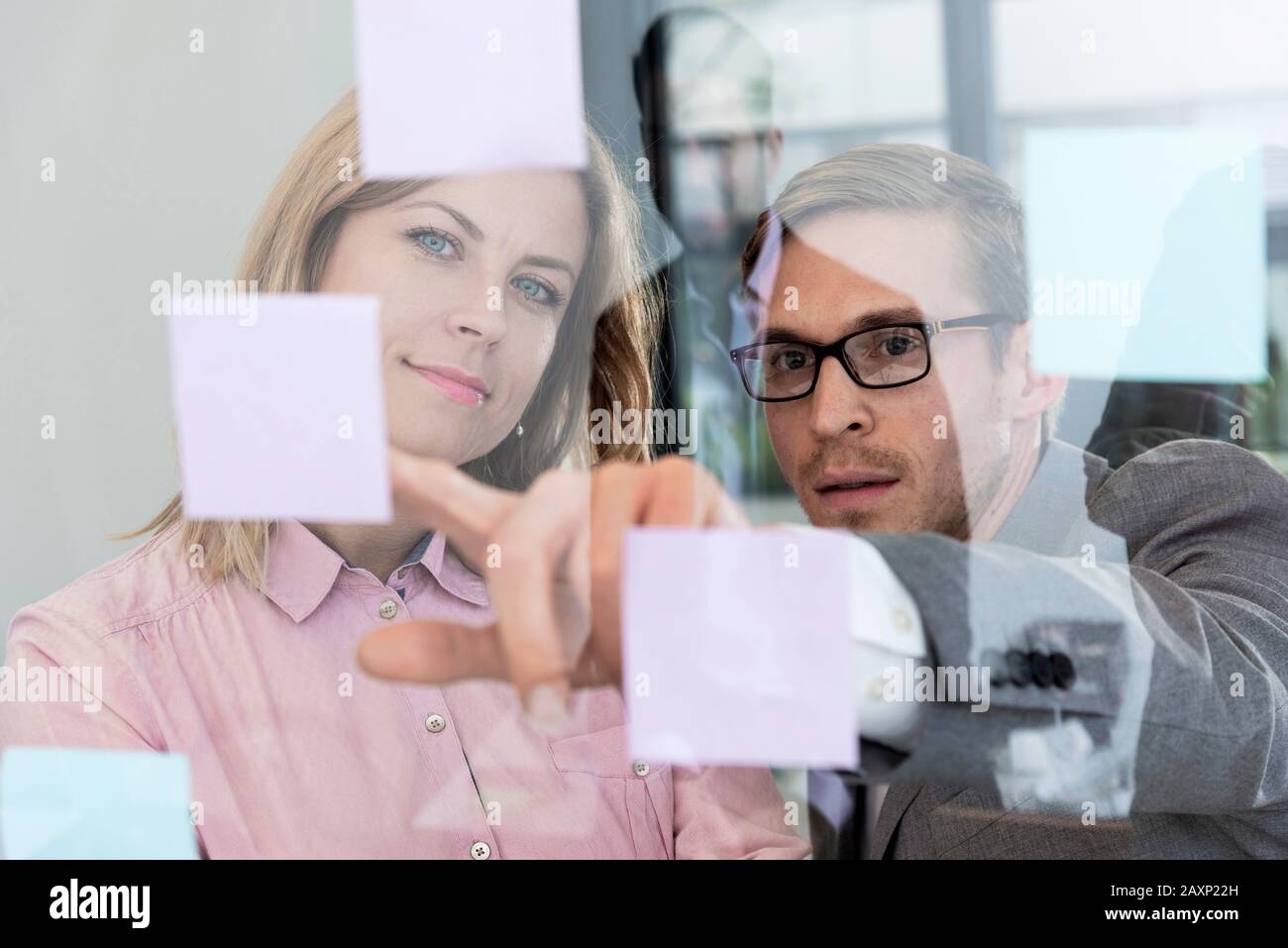 Giovane donna d'affari e giovane uomo d'affari leggono post-it in un vetro, ritratto Foto Stock