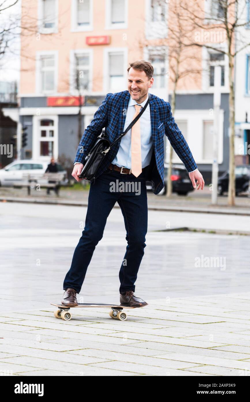 Uomo d'affari sulla strada per lavorare con skateboard Foto Stock