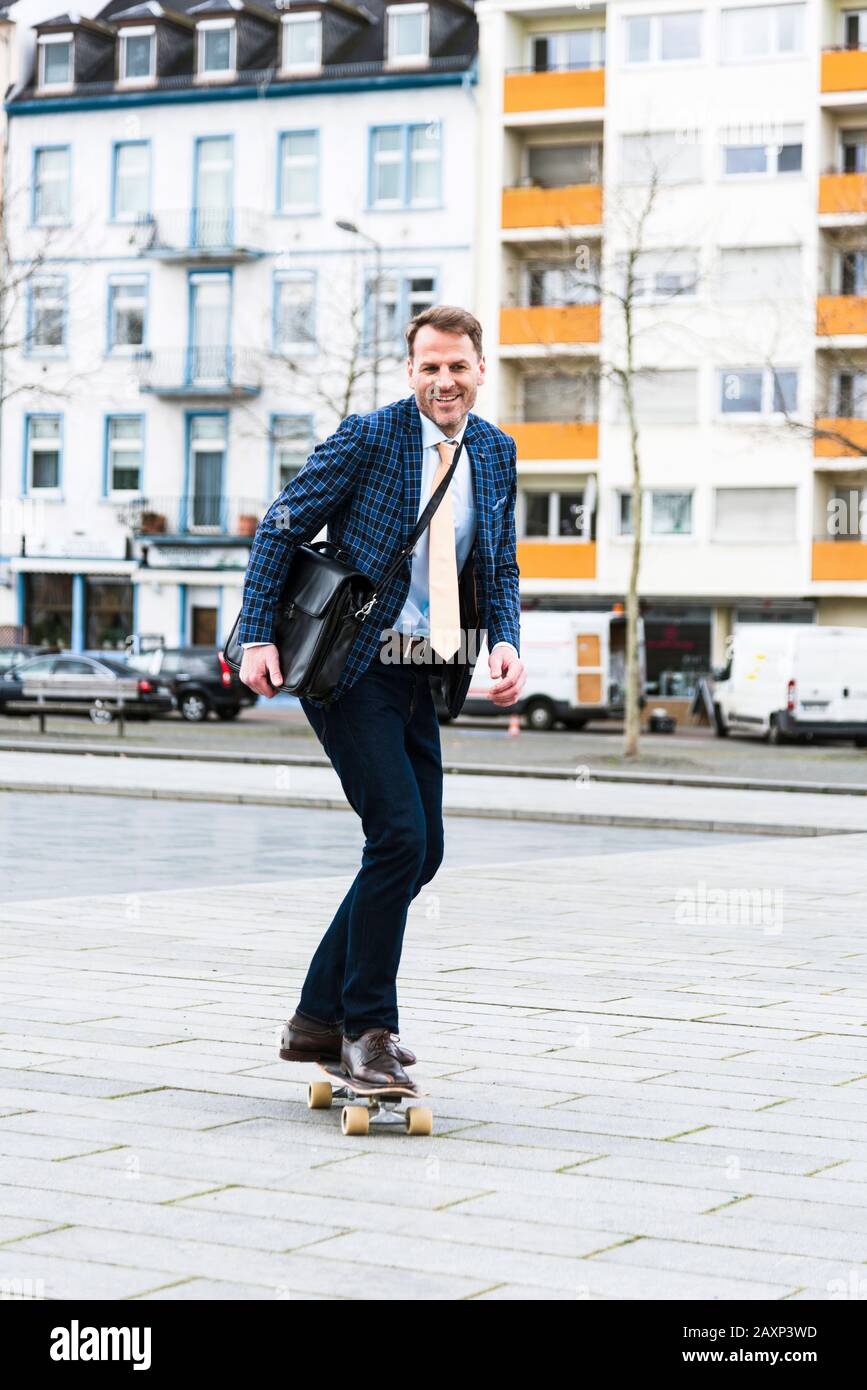 Uomo d'affari sulla strada per lavorare con skateboard Foto Stock