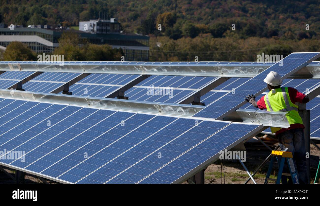 Operai che installano una serie di pannelli solari in un campo aperto nel Vermont meridionale Foto Stock