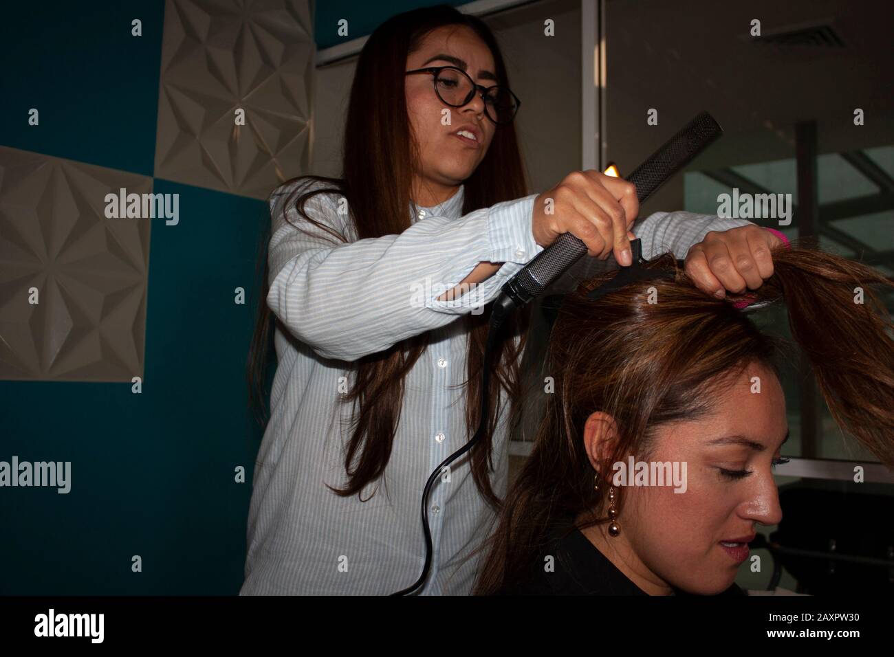 Capelli diritto stylist donna utilizza strumenti di bellezza pinza e spazzola utilizzando le sue mani per pettinare e stilizzare i capelli ambra di una donna brunetta in Messico Foto Stock