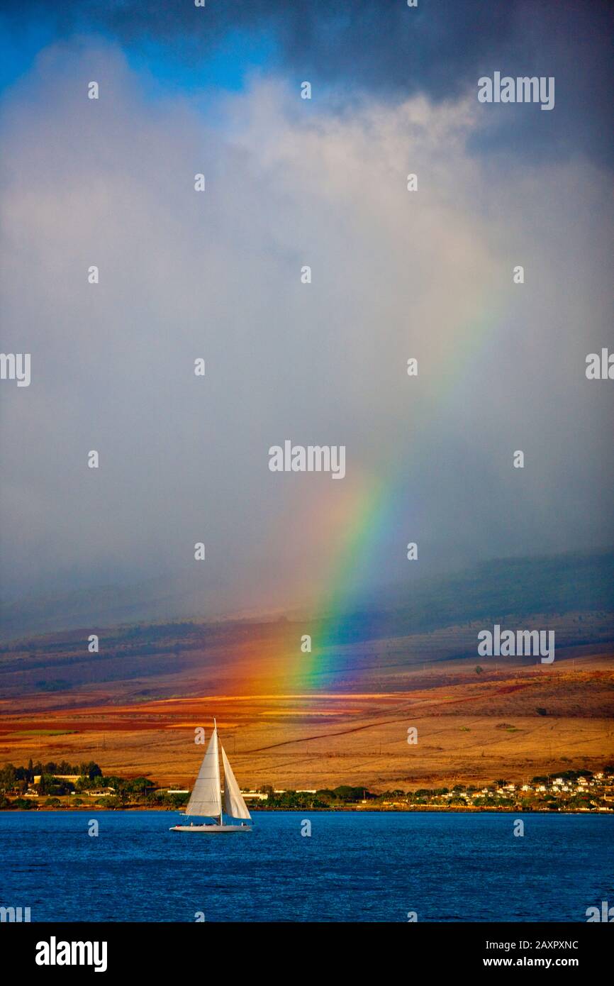 Barca a vela passando costa con un arcobaleno sullo sfondo. Foto Stock