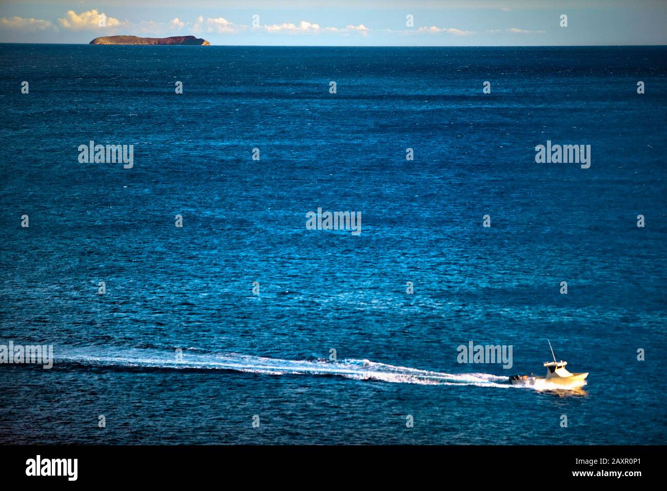 Barca da pesca si muove attraverso il mare passato un'isola all'orizzonte. Foto Stock