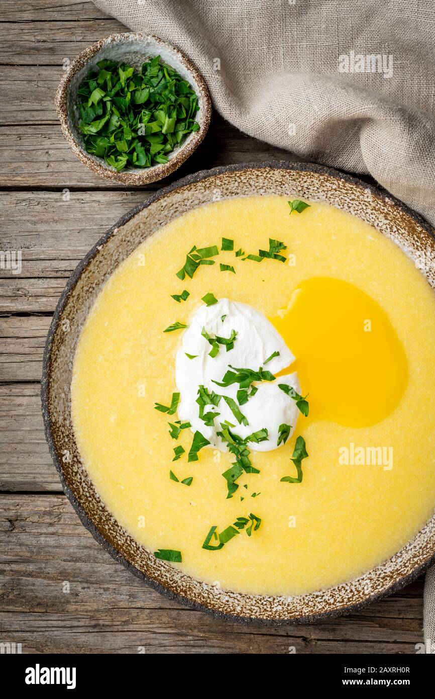 Polenta, porridge con parmigiano e uovo in camicia, verticale su vecchio sfondo di legno scuro, vista dall'alto. Cucina tradizionale italiana Foto Stock