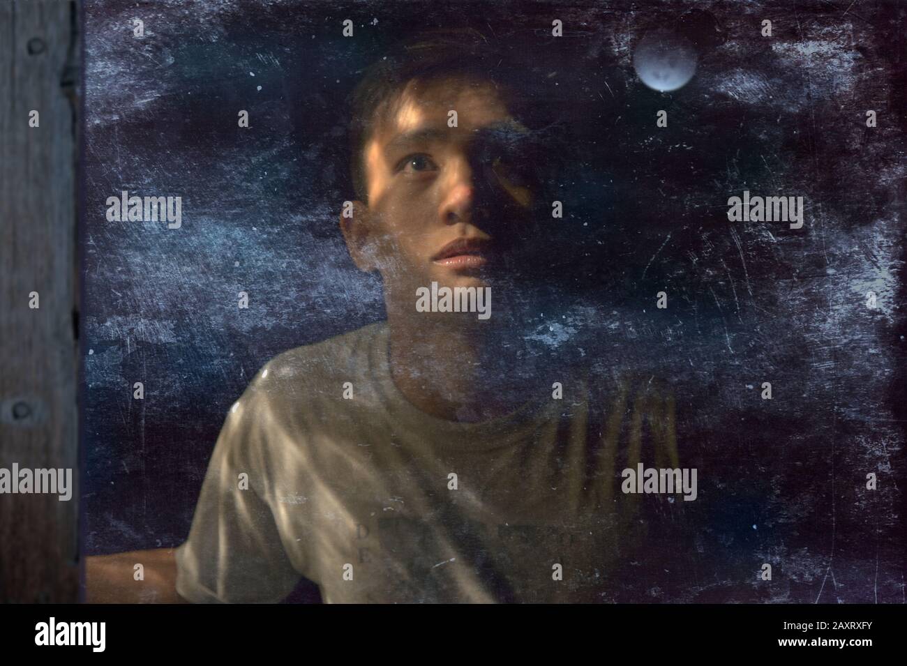 Un giovane uomo che guarda la luna attraverso una finestra sporca Foto Stock