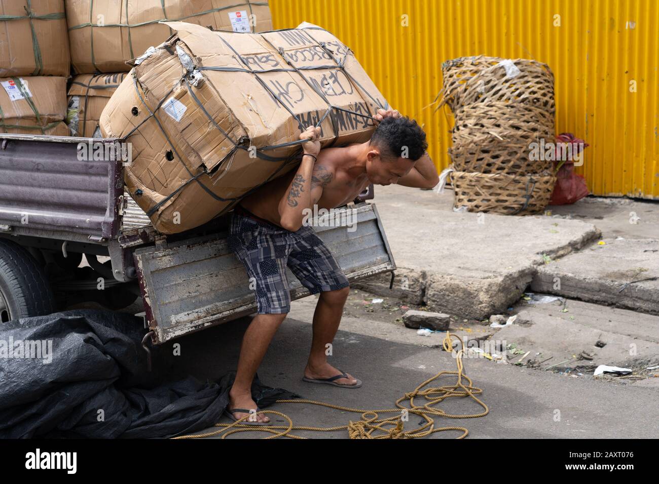 Un uomo filippino bilancia e si prepara a trasportare un carico pesante di merci all'interno di una zona di mercato di Cebu City, Filippine Foto Stock