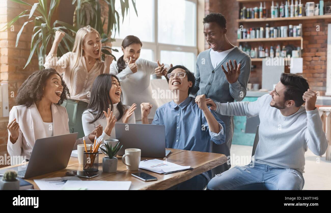 Un team aziendale multietnico che guarda lo schermo del notebook e celebra il successo Foto Stock
