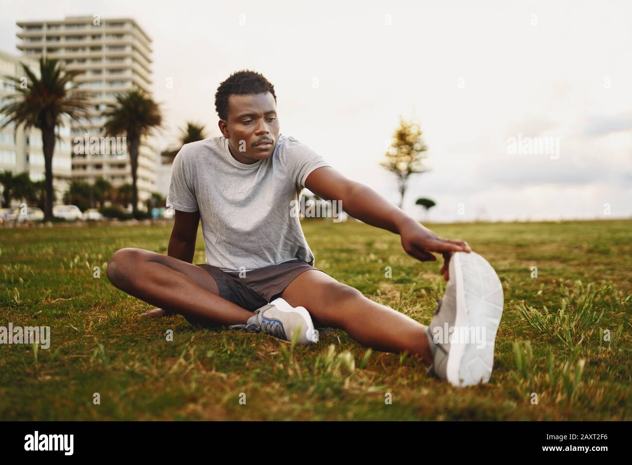 Un giovane uomo afroamericano di fitness seduto su erba verde che allunga le gambe prima di allenarsi Foto Stock