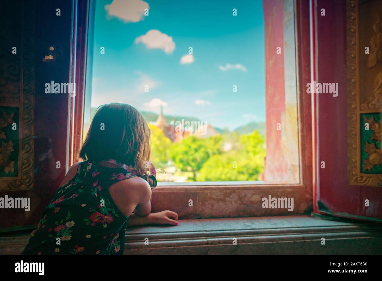 Wat Chalong, Phuket/Thailandia-15December2019: Giovane ragazza marrone capelli guardando fuori da una finestra alla grande pagoda backgr cielo nuvoloso blu e altre pagode Foto Stock