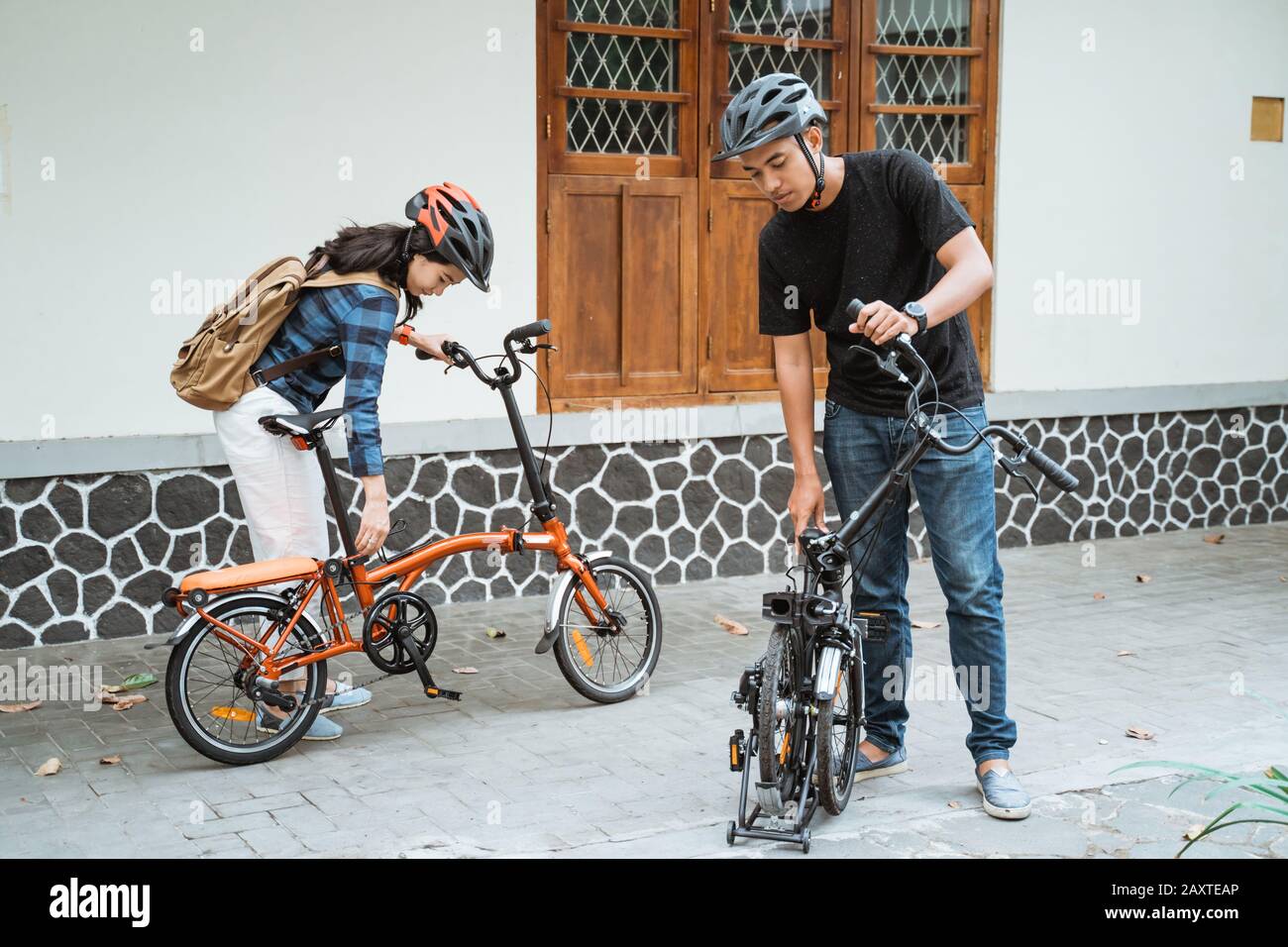 Asian coppie giovani preparare biciclette pieghevoli e indossare il casco prima di andare fuori nella parte anteriore della casa Foto Stock