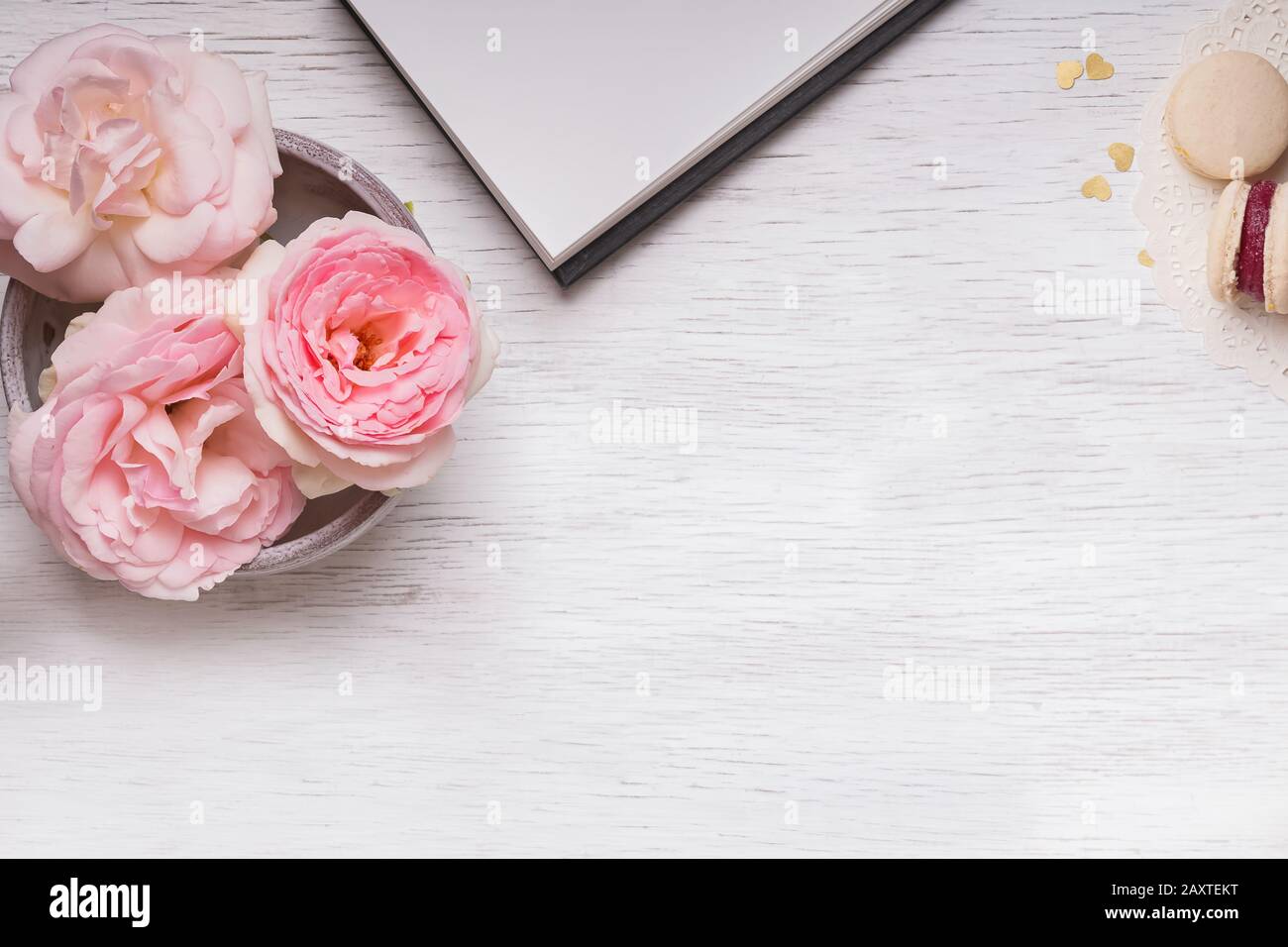 Rosa rose, blocco note, orologio e macaron su tavola di legno bianco Foto Stock