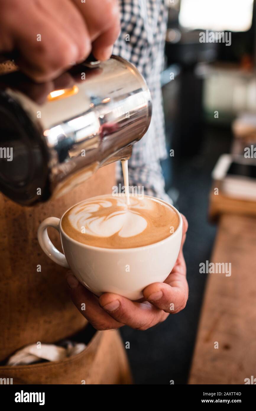 Colpo verticale di un uomo che versa il latte in un cappuccino tazza in un caffè Foto Stock