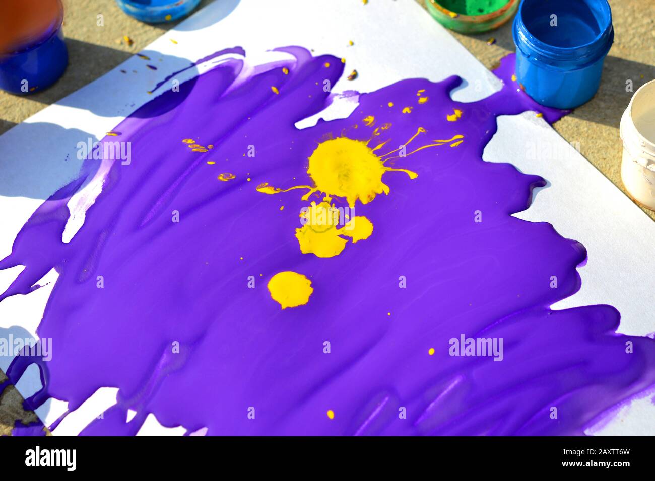 Vernice liquida viola gouache con macchie gialle su carta bianca in una giornata di sole da vicino Foto Stock