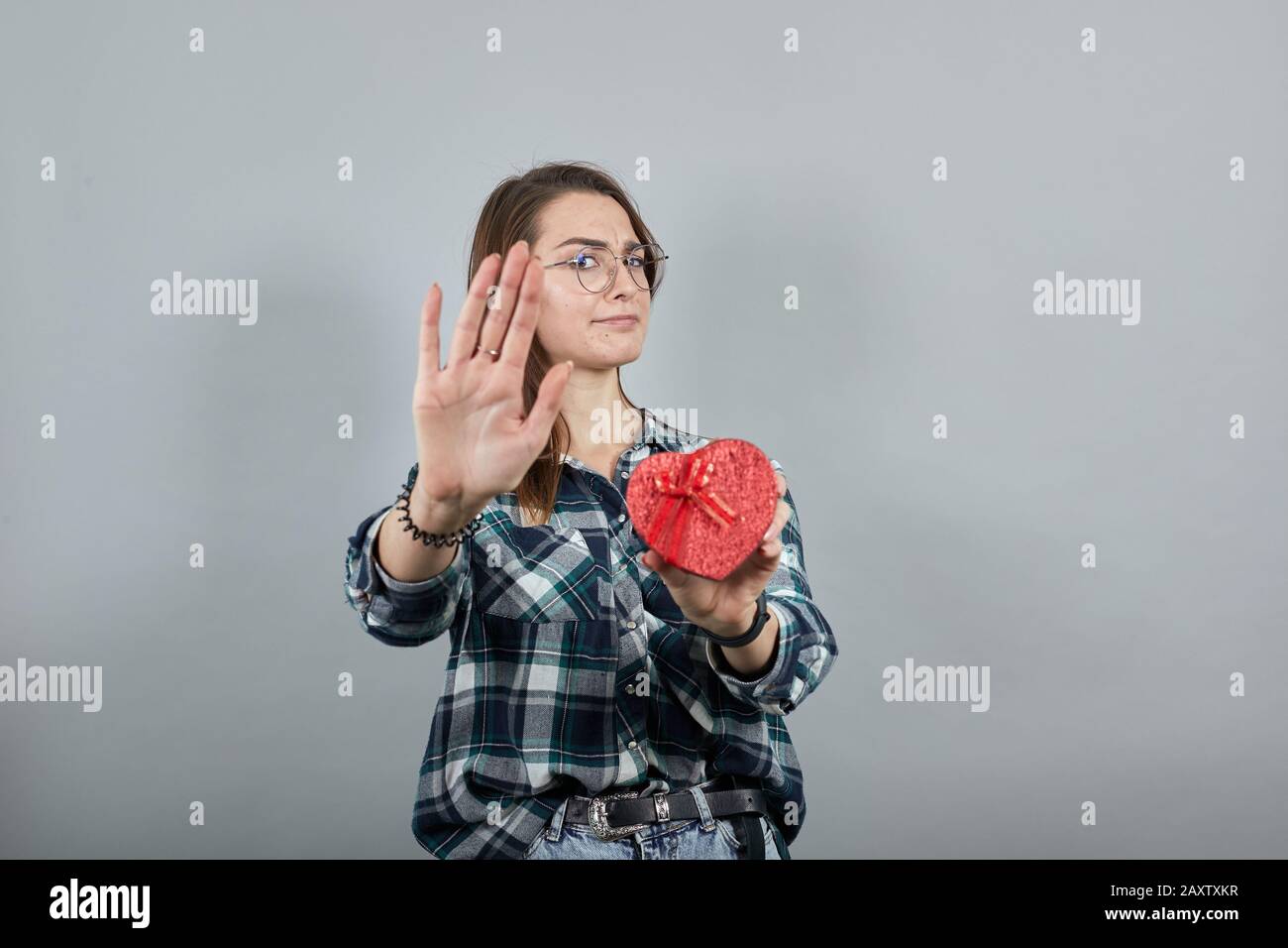 la donna insultata tiene una scatola rossa regalo sotto forma di cuore, si ferma con il palmo della mano Foto Stock