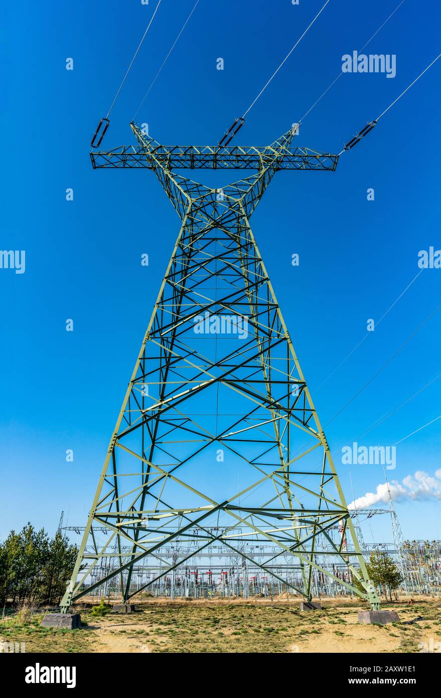 Torre elettrica in metallo verde su un campo con una stazione di trasformatore sullo sfondo Foto Stock