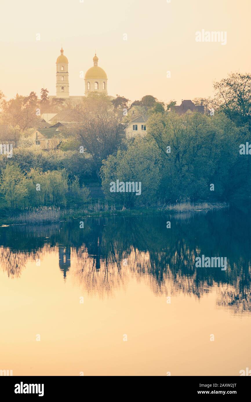 Chiesa e case al tramonto, alba e riflessione in acqua Foto Stock