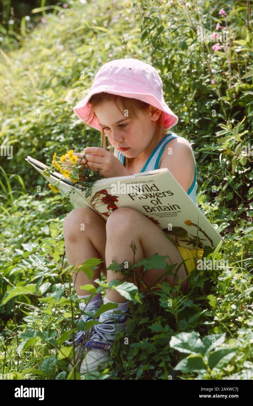 giovane ragazza seduta tra fiori selvatici che identificano i fiori di un libro Foto Stock