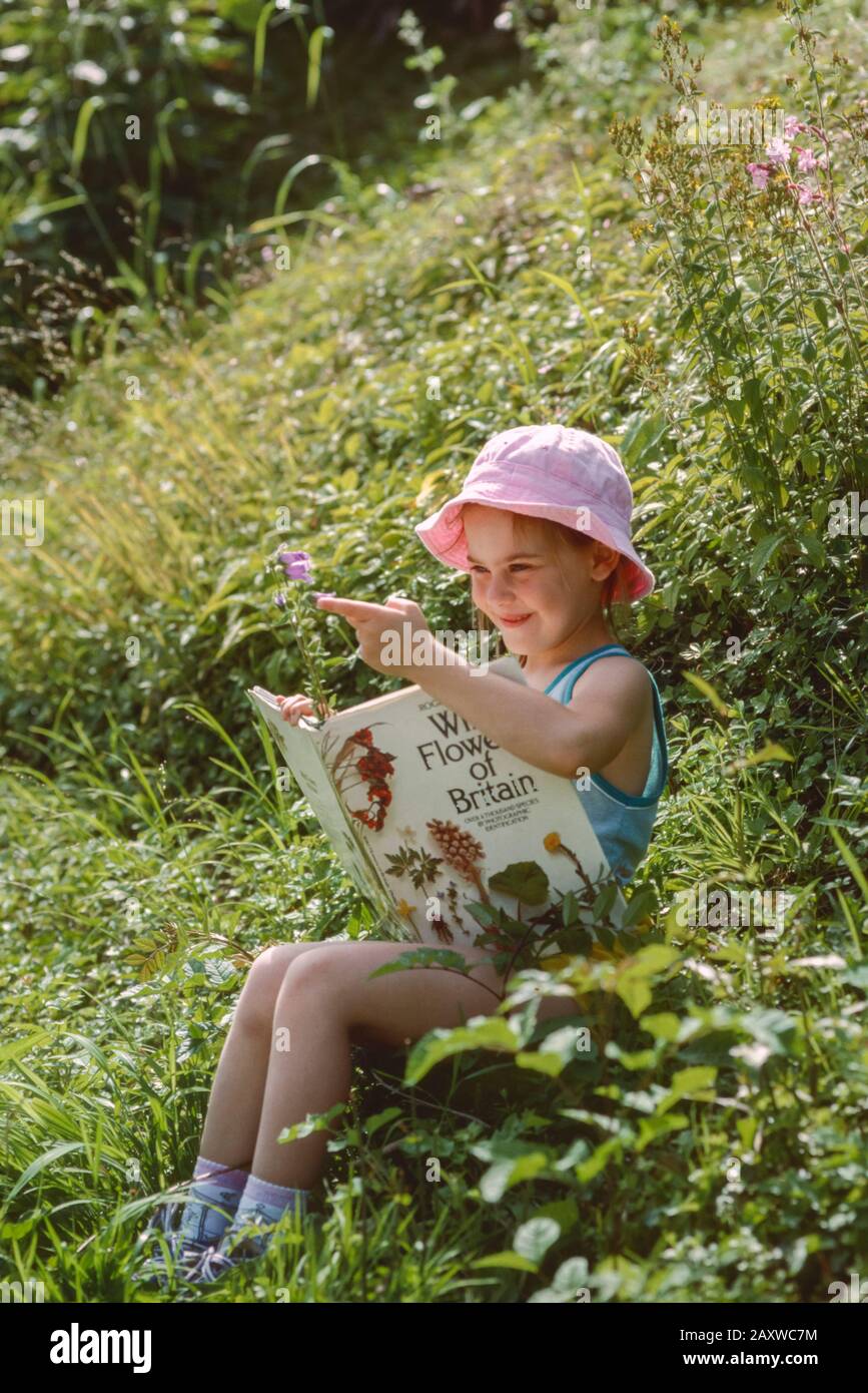giovane ragazza seduta tra fiori selvatici che identificano i fiori di un libro Foto Stock