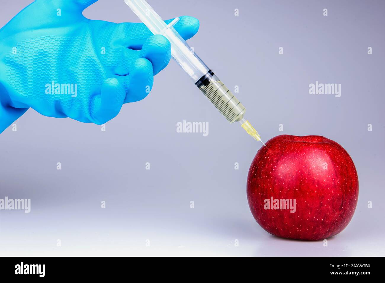 Mela rossa geneticamente modificata con siringhe su sfondo bianco.siringa medica per iniezione di OGM Foto Stock