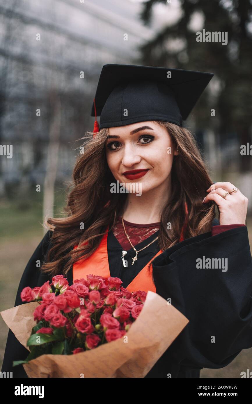 Felice giovane studente di laurea in abito di laurea che tiene bouquet di fiori mentre si trova nel campus Foto Stock