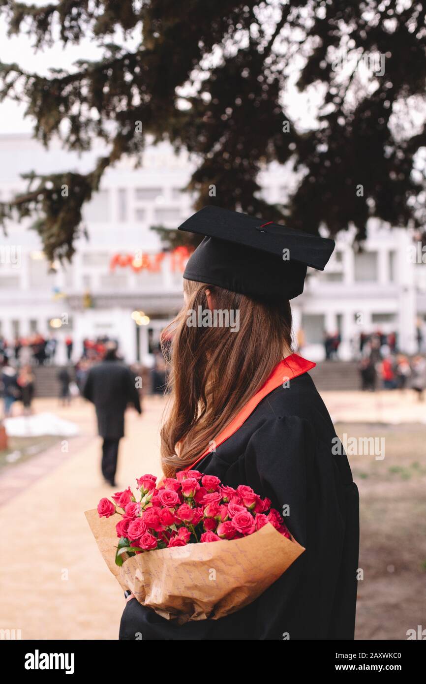 Vista posteriore della studentessa laureata in possesso di un mazzo di fiori mentre si trova nel campus durante la cerimonia di laurea Foto Stock