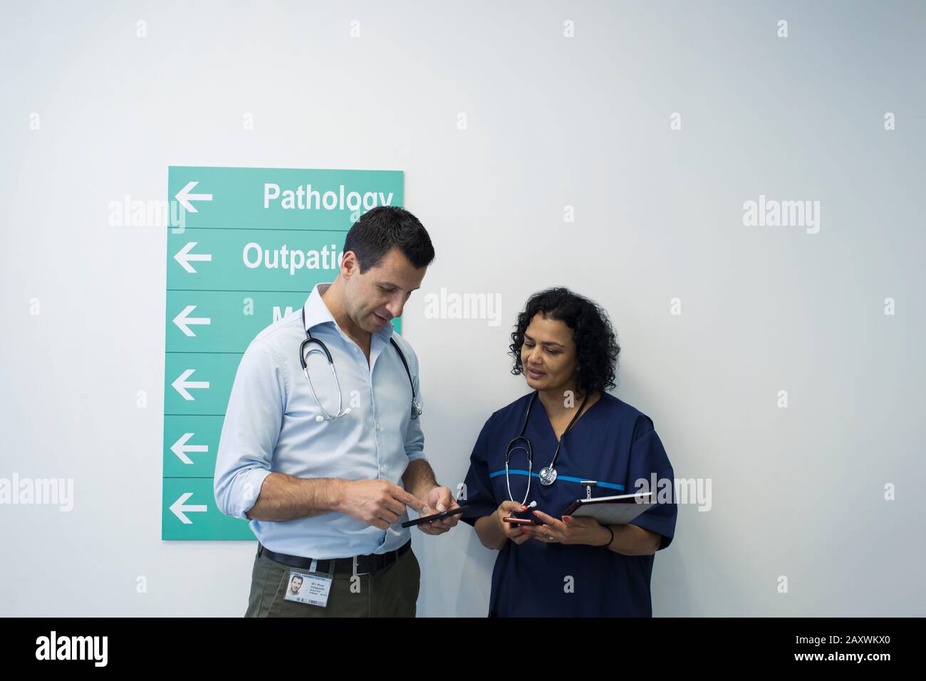 Medici con smartphone che parlano nel corridoio ospedaliero Foto Stock