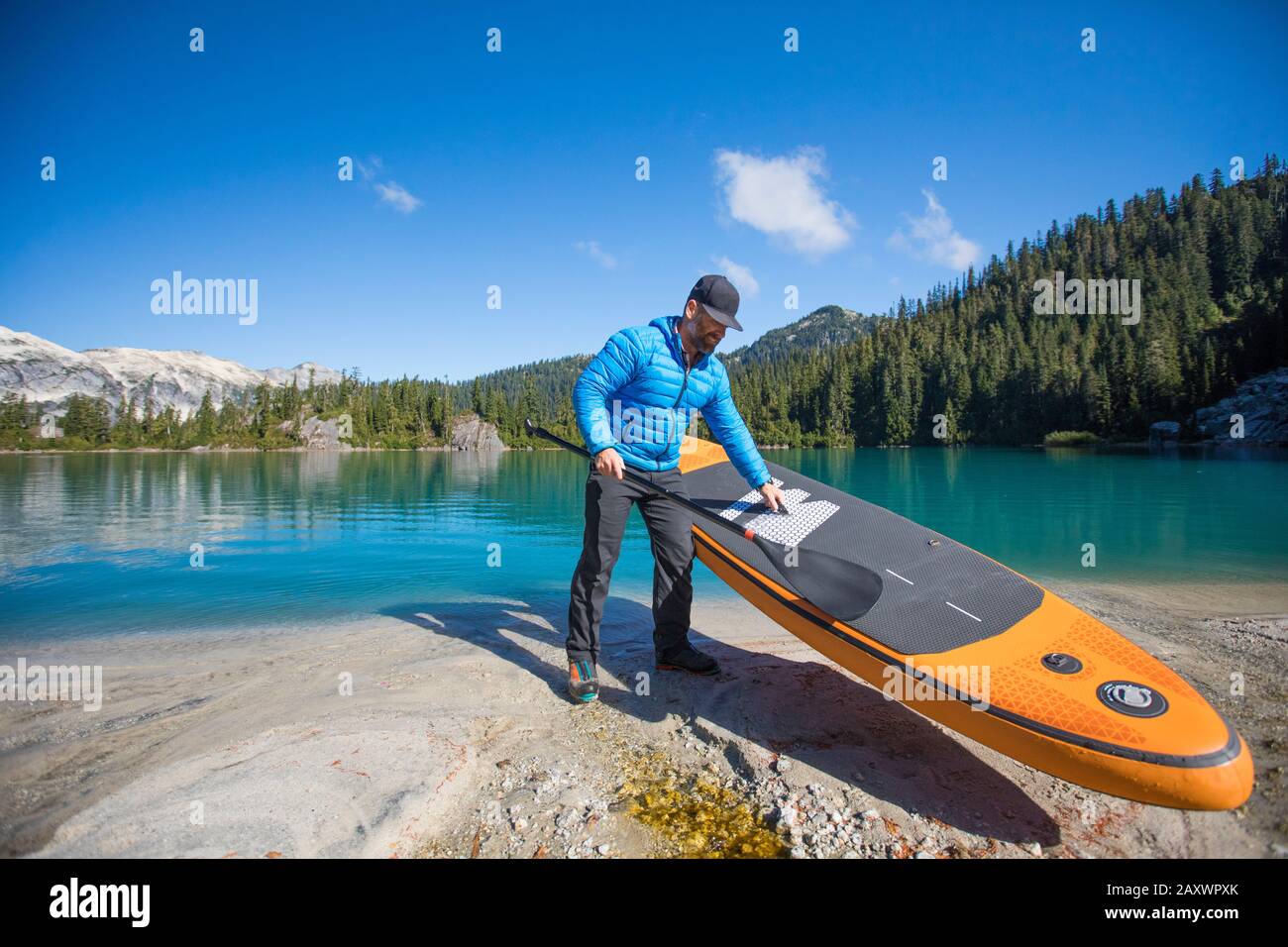 L'uomo avventuroso si prepara ad usare SUP sul remoto lago alpino. Foto Stock