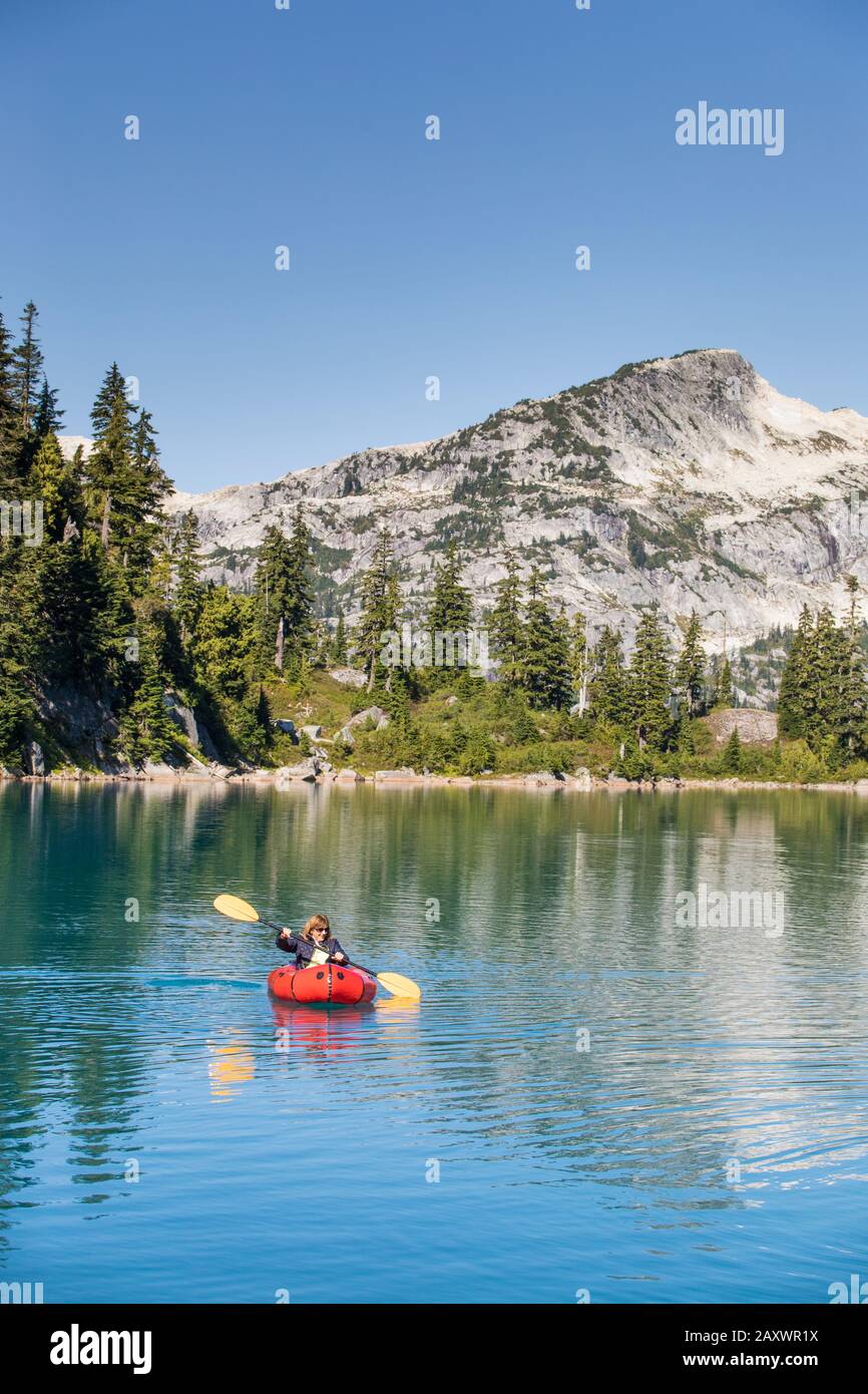 Donna pensionato pagaiare sul lago di montagna remoto. Foto Stock