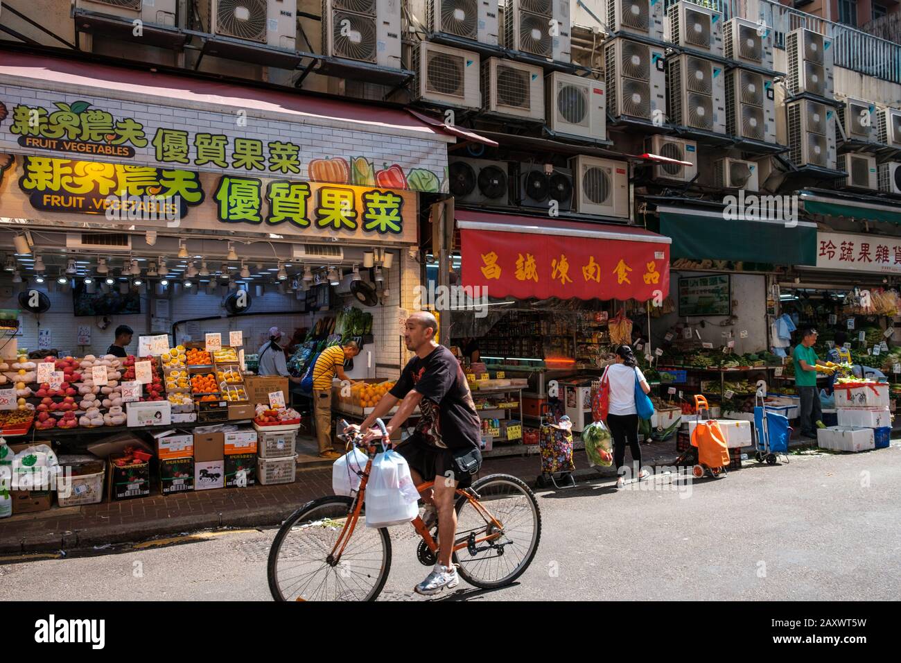 Hong Kong, novembre 2019: Uomo in bicicletta con borse che passano davanti ai negozi del mercato alimentare di Hong Kong, Foto Stock