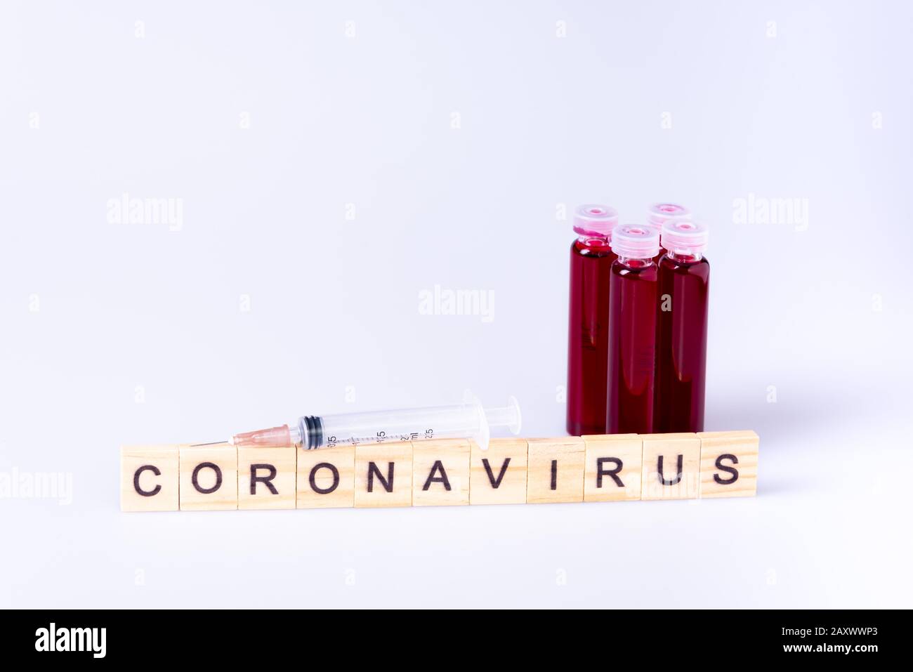 Le lettere di coronavirus si presentano con una piccola provetta con sangue e iniezione di ago su sfondo bianco Foto Stock