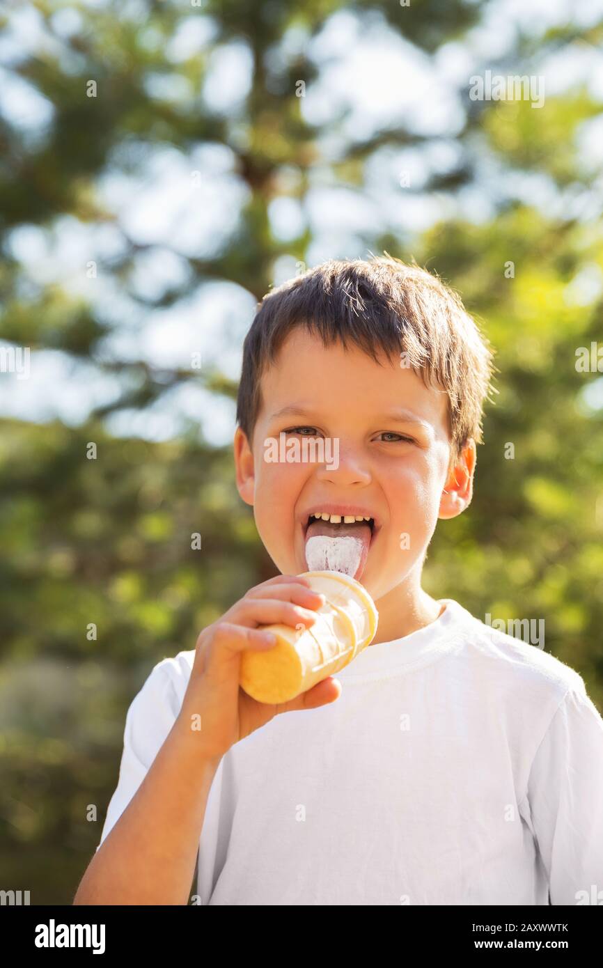 Bambino 5 anni in t-shirt bianca con gelato in estate all'aperto. Gelato a base di lecca per bambini in una tazza di waffle Foto Stock