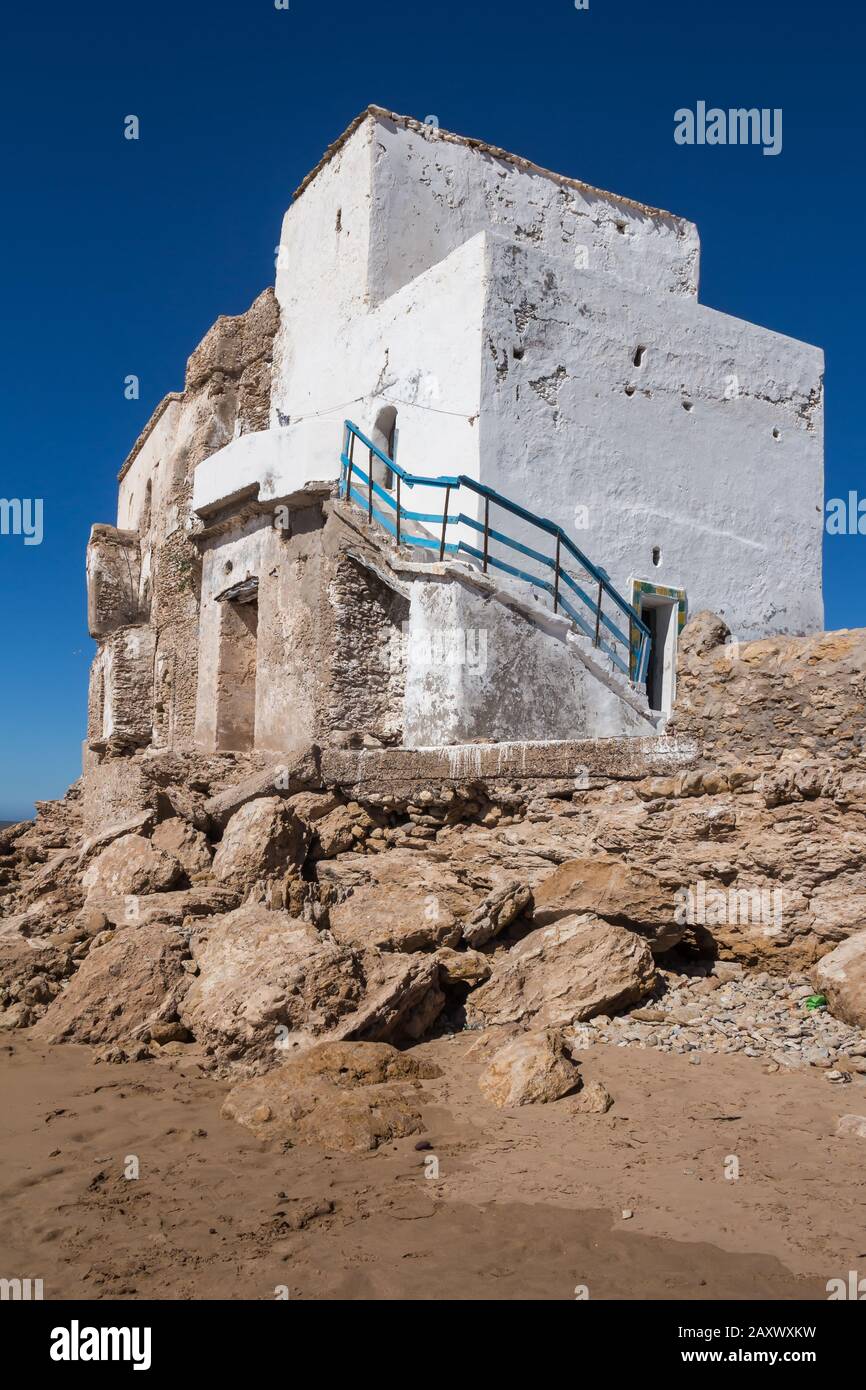 Edificio bianco abbandonato, costruito sulle rocce sulla costa dell'Oceano Atlantico. Cielo blu brillante. Sidi Kaouki, Marocco. Foto Stock