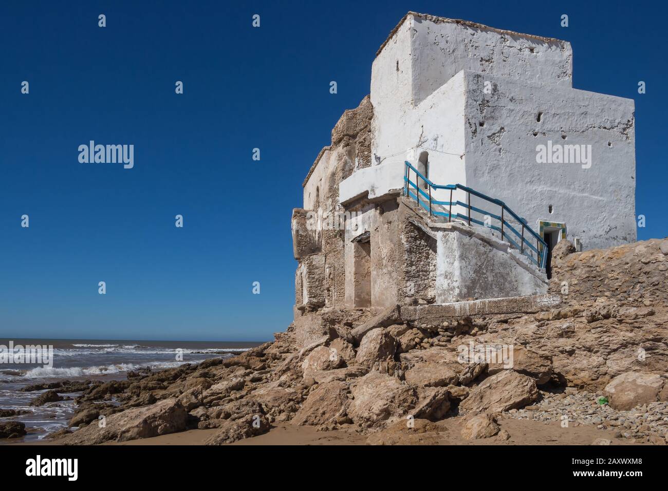 Edificio bianco abbandonato, costruito sulle rocce sulla costa dell'Oceano Atlantico. Cielo blu brillante. Sidi Kaouki, Marocco. Foto Stock