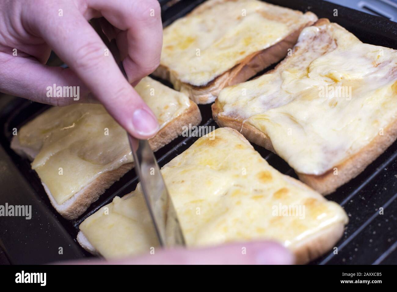Un paio di mani da una persona non identificabile che prepara quattro fette quadrate di pane alla griglia con formaggio fuso Foto Stock