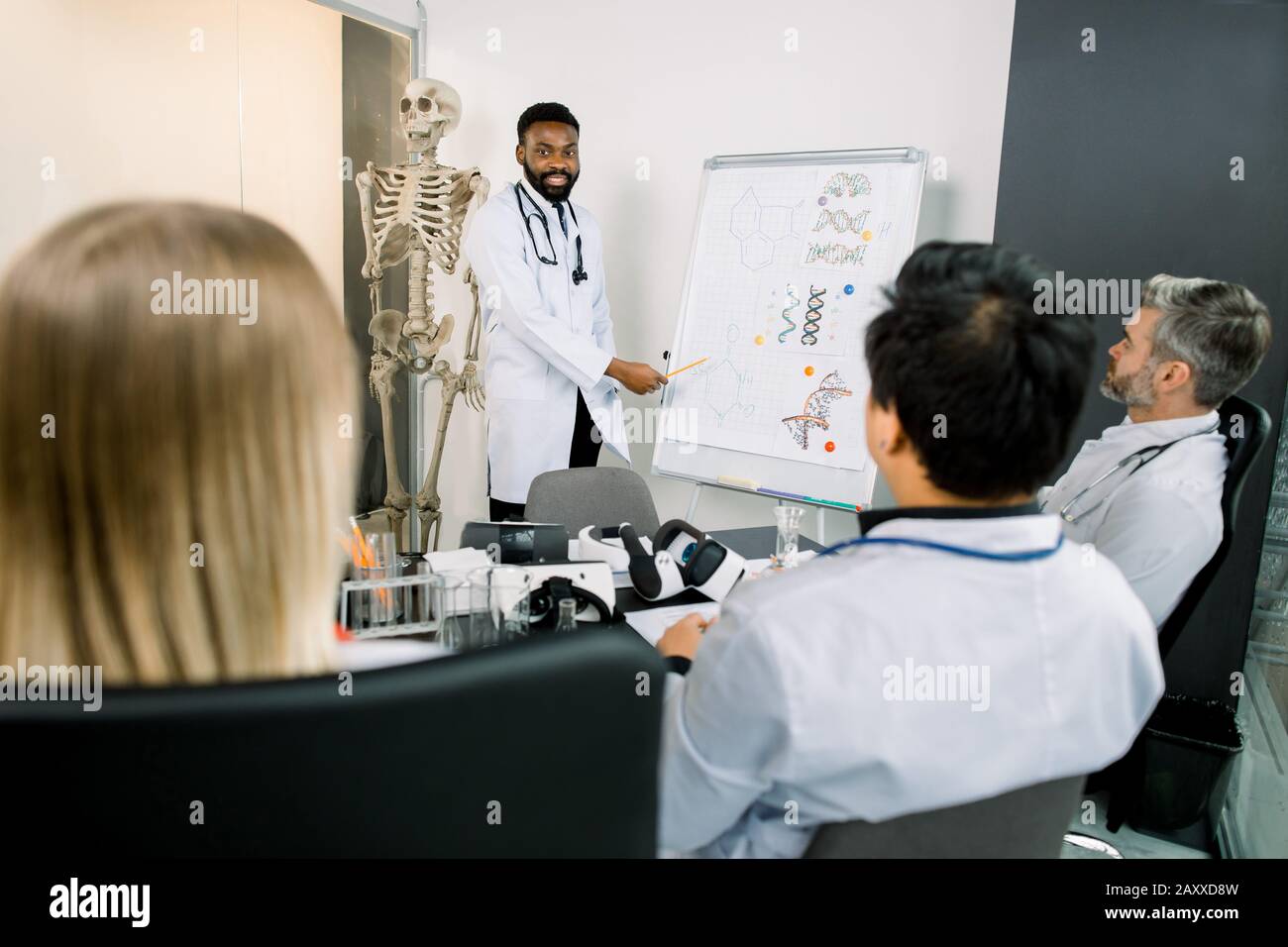 Bel giovane scienziato medico africano indossando cappotto bianco in piedi vicino a lavagna a fogli mobili e dando la presentazione di molecole biochimiche, nuovo Foto Stock