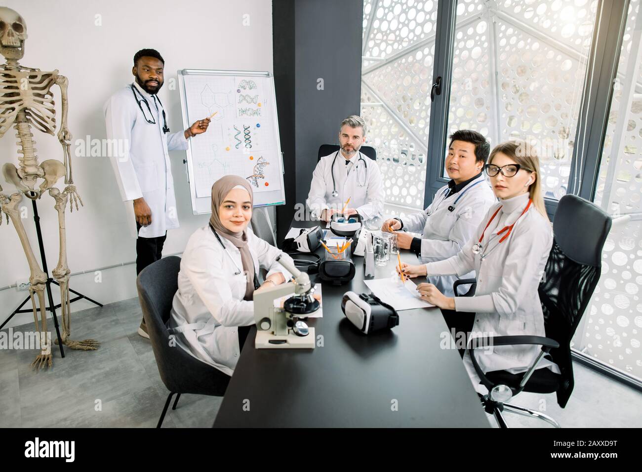 Ritratto di professore di mezza età con gruppo di studenti multietnici, seduto al tavolo in un laboratorio o in un'aula moderna. Medico chimico africano Foto Stock