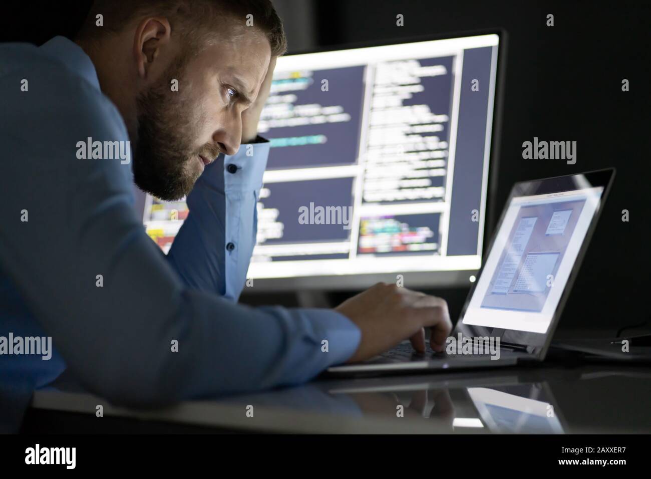 Preoccupato per il programmatore a lavorare fino a tarda notte su più schermi di computer Foto Stock