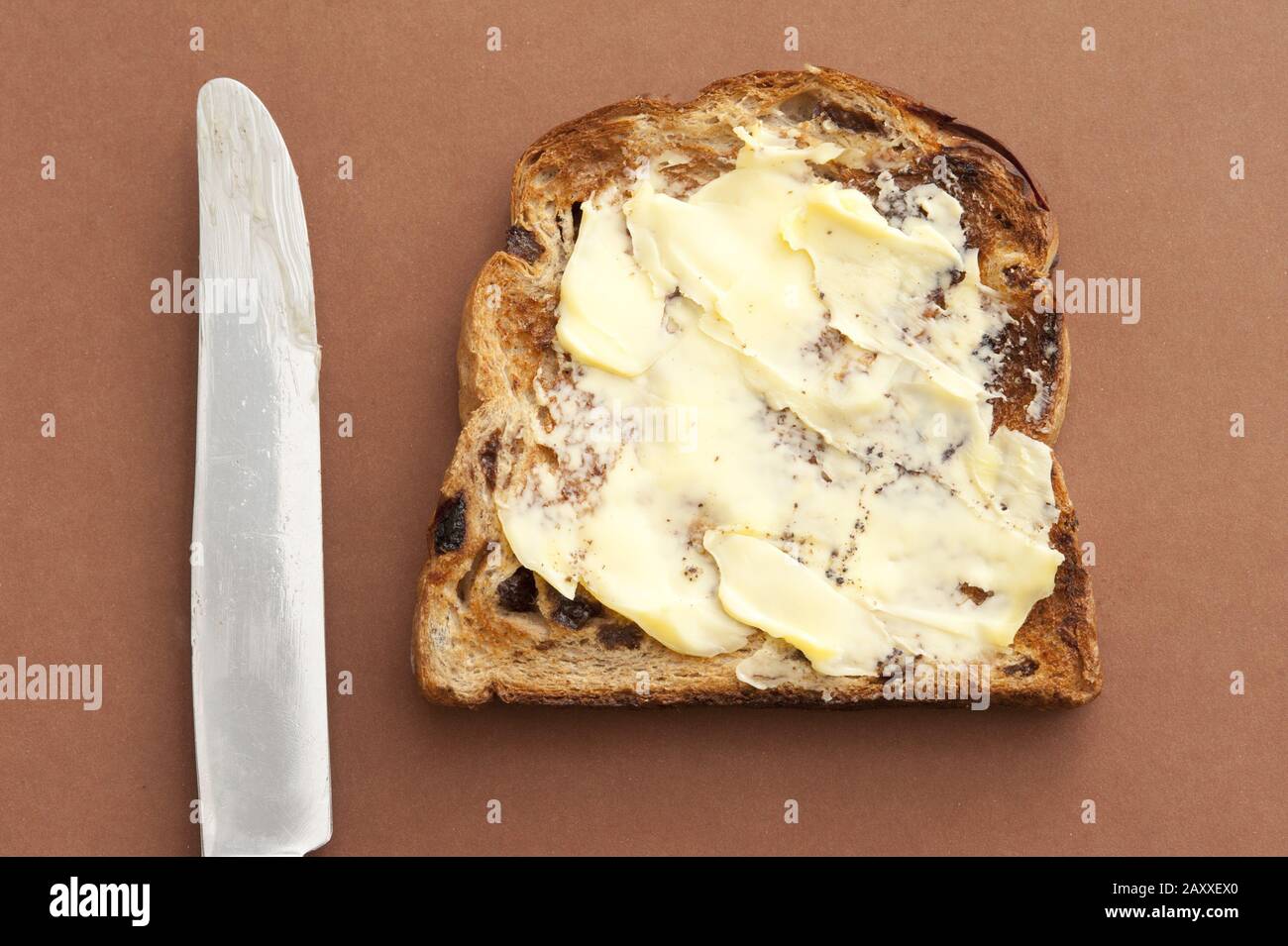 Primo piano di deliziosa fetta di pane con burro spalmabile e coltello su fondo marrone. Dall'alto Foto Stock
