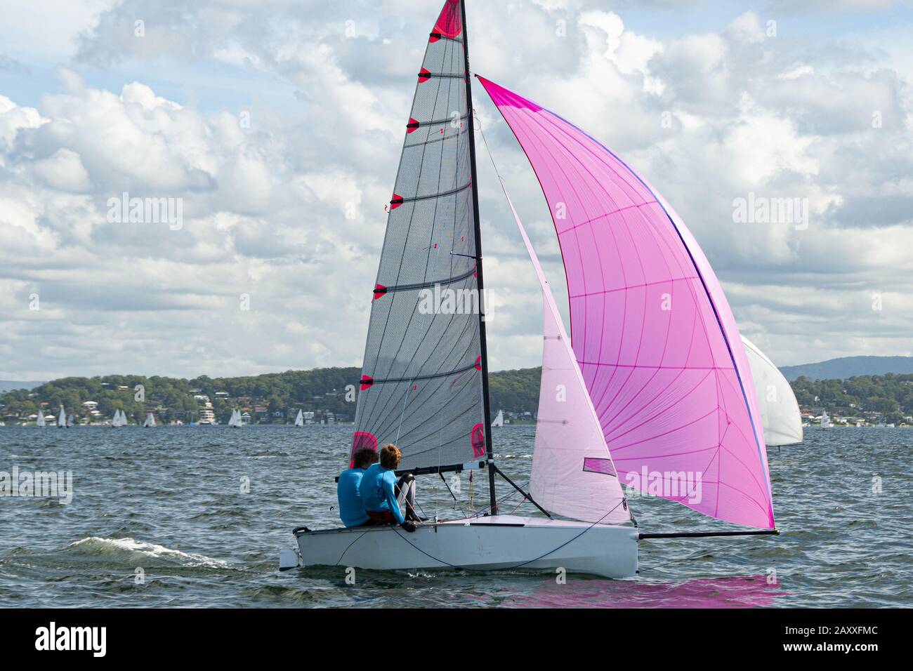 Due ragazzi della scuola che navigano su una piccola barca a vela con un vivace spinnaker rosa per divertirsi e in competizione. Lavoro di squadra da parte dei marinai junior che corrono su s. Foto Stock